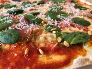 Sprød, tyndbundet pizza med parmesan, mozzarella, serranoskinke, grøn pesto, passata og pinjekerner
